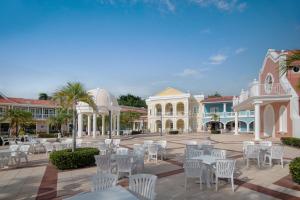 un patio con mesas blancas, sillas y edificios en Bahia Principe Grand La Romana - All Inclusive en La Romana