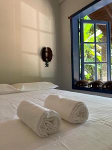 two towels on a white bed with a window at Pousada Maikai Garden in Porto Belo