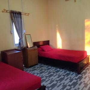 Karang Besi Losmen في Biha: غرفة بسريرين مع شراشف حمراء ونافذة