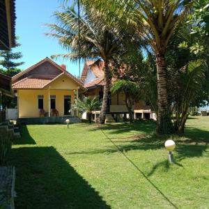 una casa amarilla con palmeras en el patio en Karang Besi Losmen en Biha