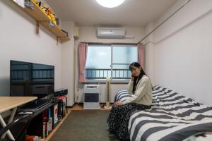 uma mulher sentada numa cama num quarto em Almaz Place #205 em Sapporo