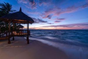 einen Strand mit Pavillon und das Meer bei Sonnenuntergang in der Unterkunft Banyan Tree Vabbinfaru in Male City