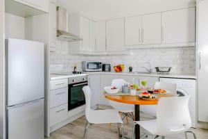 a white kitchen with a wooden table and white chairs at #7 six sleeps Zone1 - BrickLane in London