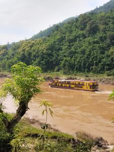 a yellow boat on a river with a mountain at Dorm Riverside in Pakbeng