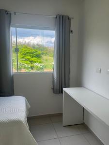 ein weißes Schlafzimmer mit einem Fenster und einem weißen Bett in der Unterkunft Condomínio Villa Verde Triunfo in Triunfo