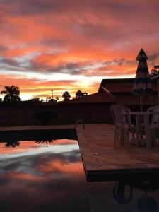 een zonsondergang boven een zwembad met stoelen en een parasol bij Casa com piscina no interior em condomínio fechado in Quadra
