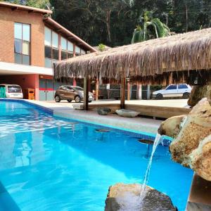 a swimming pool with a thatch roof at EcoHotel Vale do Sol in Embu