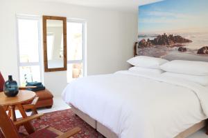 Un dormitorio blanco con una cama grande y una mesa en Nivenia Beach House en Bettyʼs Bay