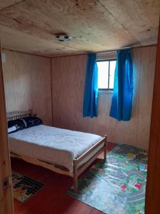Schlafzimmer mit einem Bett mit blauen Vorhängen und einem Fenster in der Unterkunft Compu alto in Quellón