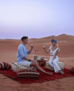a man and woman sitting in the desert with drinks at Desert Berber Camp in Merzouga