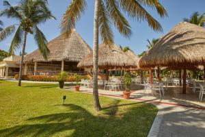 een restaurant met tafels en rieten parasols en palmbomen bij Bahia Principe Grand Coba - All Inclusive in Akumal