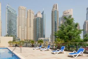 a row of lounge chairs next to a swimming pool with tall buildings at Chic Apartment Dubai Marina in Dubai