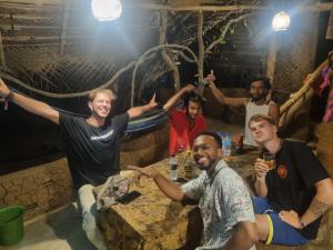 Un gruppo di uomini seduti intorno a un tavolo con le braccia in aria di Sigiriya Rastha Hostel a Sigiriya