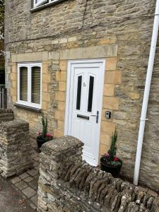 a stone house with a white door and a stone wall at The Old Bakery in South Cerney
