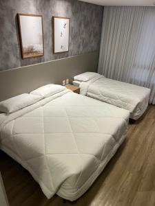 2 camas en una habitación de hotel con sábanas blancas en Hotel das Américas, en Balneário Camboriú