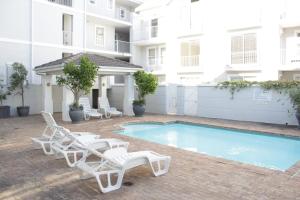 a swimming pool with white lounge chairs next to a building at Tranquil Haven with Uninterrupted Power, a Serene Oasis in the Heart of Cape Town in Cape Town