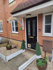 a house with a black door and two potted plants at Cozy House, Garden, Free Parking, Opposite Train station with Disneyplus & Netflix included in West Thurrock