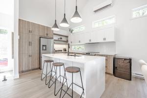 a kitchen with white cabinets and a white island with bar stools at Le Montagnard Spa Sauna Piscine Privés in Brownsburg