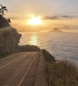 a road next to the ocean with the sun setting at Casa Temporada in Rio de Janeiro