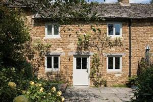 a brick house with a white door in front of it at Two Rose Walk Cottage Cotswolds in Moreton in Marsh