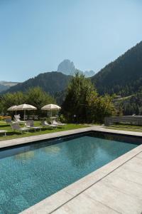 a swimming pool with chairs and umbrellas at Diamant Spa Resort in Santa Cristina Gherdëina