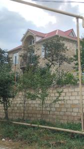 a house on a brick wall with trees in front of it at GUEST House in Qusar