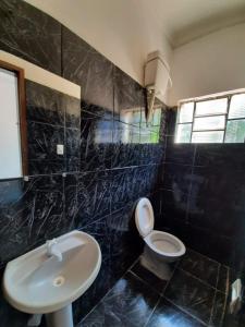uma casa de banho com azulejos pretos, um WC e um lavatório. em Hotel Perola Ltda em Cuiabá
