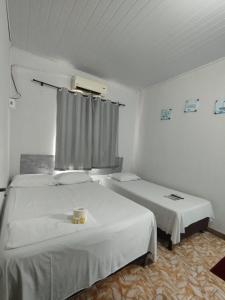 a white room with two beds and a window at Hotel Perola Ltda in Cuiabá