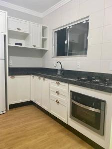 uma cozinha com armários brancos, um lavatório e um micro-ondas em Residencial Bejaju 03 em Bombinhas