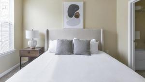 Landing Modern Apartment with Amazing Amenities (ID1174X415) في ماديسون: غرفة نوم مع سرير أبيض و كومودينو مع مصباح