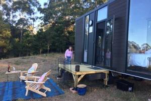 una mujer parada fuera de una pequeña casa negra en White Jacaranda Tiny House, en Maleny