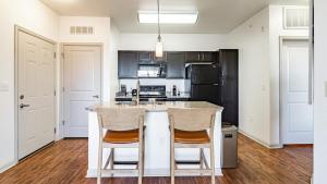kuchnia z czarnymi szafkami i biała wyspa z dwoma krzesłami w obiekcie Landing Modern Apartment with Amazing Amenities (ID7813X12) w Aurorze