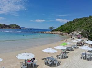 ein Strand mit Stühlen und Sonnenschirmen und Menschen im Wasser in der Unterkunft Mar Y Suites in Cabo Frio