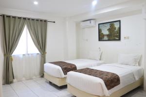 two beds in a hotel room with a window at Hotel Netral Jombang in Jombang