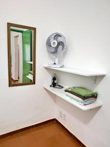 un mur blanc avec une étagère, un ventilateur et un miroir dans l'établissement Casa Completa e Independente em Cabo Frio - RFV106, à Cabo Frio