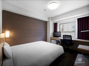 仙台市にあるダイワロイネットホテル仙台のベッド、デスク、コンピュータが備わるホテルルームです。