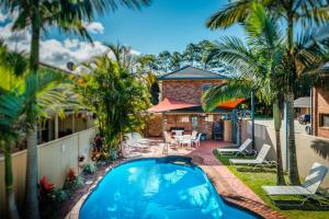 una piscina di fronte a una casa con palme di Park Beach Resort Motel a Coffs Harbour