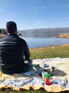 un homme assis sur une couverture de pique-nique en regardant un lac dans l'établissement Cabañas Ezequiel, à Villa Carlos Paz