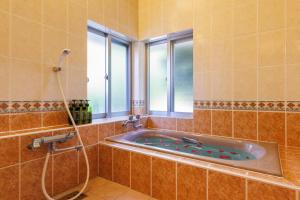 a bathroom with a tub with a shower and a window at Cottage Muinochichi in Motobu