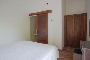 a bedroom with a white bed and a wooden door at Rumah Kecil Sanur in Sanur