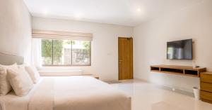 a white bedroom with a large bed and a television at D'Green Kuta Managed by ARM Hospitality in Legian