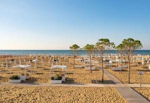 a beach with white chairs and umbrellas on the sand at Well equipped apartment in Bibione - Beahost - in Bibione +65 photos