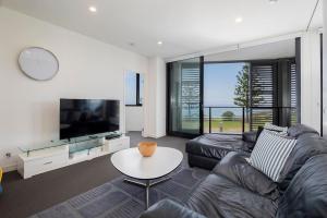 a living room with a couch and a tv and a table at The Sandpiper - A Newy Beachfront Beauty in Newcastle