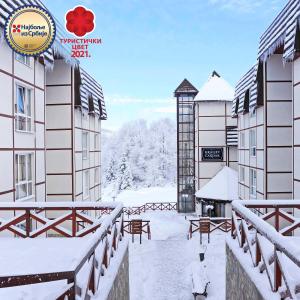 a snow covered courtyard of a building with a clock at Hotel Kraljevi Čardaci in Kopaonik