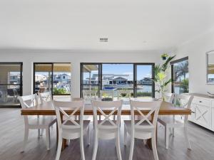 a dining room with a wooden table and white chairs at Mariner's Cove Luxury Canal Home in Mandurah
