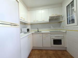 Una cocina con gabinetes blancos, un fregadero y un microondas. en Urbanización San bruno II en segunda planta., en Isla Canela