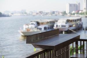 a black bench sitting on a balcony with boats in the water at NORN Riverside Bangkok Hotel - นอนริมน้ำ in Bangkok