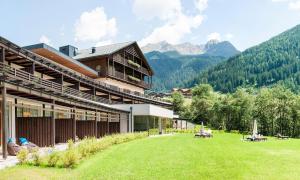a building with a grassy yard with mountains in the background at La Casies Mountain Living Hotel in Santa Maddalena