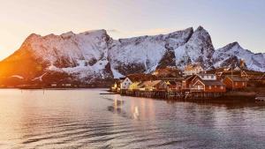 a village on the water with snow covered mountains at Fjordview Ryten 2 Retreat in Sund