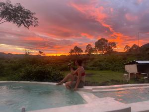 two people sitting in a pool watching the sunset at Triangular house and hot spring in Kubupenlokan